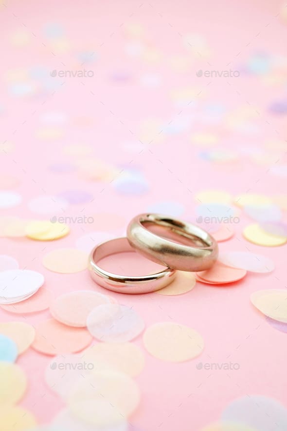 Wedding Rings On Pink Pastel Background With Paper Confetti And